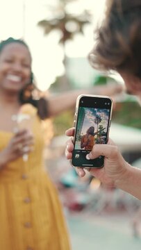 VERTICAL VIDEO: Close-up of a man taking a picture of a woman on a mobile phone. Closeup, smiling woman eating ice cream and filming it with smartphone on urban city background. Backlight