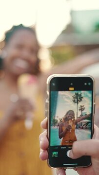 VERTICAL VIDEO: Close-up of a man taking a picture of a woman on a mobile phone. Closeup, smiling woman eating ice cream and filming it with smartphone on urban city background. Backlight