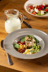 Closeup of cold soup okroshka with beef, vegetables and kefir served in a white bowl, selective focus. Summer, cold soup with cucumber, radish, egg, potatoes and fresh herbs seasoned with kefir.