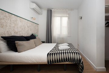 bedroom with double bed with matching blanket with cushions, curtains on the window and air conditioner on the wall