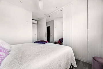 bedroom with double bed with white bedspread, and built-in wardrobe with white doors and wall-to-wall mirror
