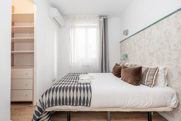 bedroom with double bed with matching blanket with cushions, net curtains and curtains on the window, dressing room with drawers and shelves and wall with decorative paper