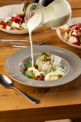 Closeup of cold soup okroshka with beef, vegetables and kefir served in a white bowl, selective focus. Summer, cold soup with cucumber, radish, egg, potatoes and fresh herbs seasoned with kefir.