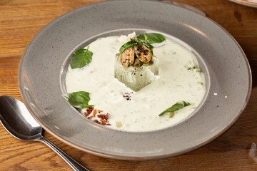 Closeup of cold soup okroshka with beef, vegetables and kefir served in a white bowl, selective focus. Summer, cold soup with cucumber, radish, egg, potatoes and fresh herbs seasoned with kefir.