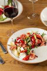 Prosciutto crudo ham salad with mozzarella cheese and arugula on a plate. Bright background. Top view. Copy space