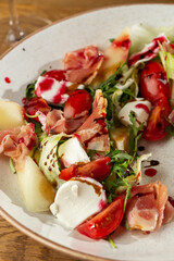 Prosciutto crudo ham salad with mozzarella cheese and arugula on a plate. Bright background. Top view. Copy space