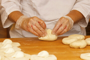 The woman in the picture is making stuffed pies. Hands in protective gloves wraps the curd filling...