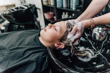 Woman applying shampoo and massaging client's hair. A woman washing her hair at a hairdresser.