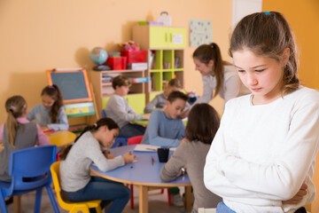 Portrait of sad schoolgirl and children drawing in classroom