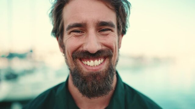 Close-up portrait of a smiling man with a beard on the embankment, on a yacht background. Frontal closeup of happy young hipster male looking at camera