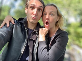 cheerful adult French man and blonde woman making faces surprised and laughing looking at the...