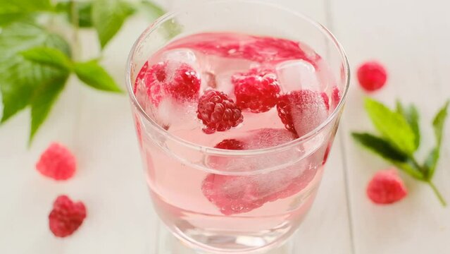 Raspberry summer cocktail.Raspberrys falls into glass with raspberry pink drink on a white wooden table.Splashes and drops of a refreshing cocktail.Summer drink.4k footage