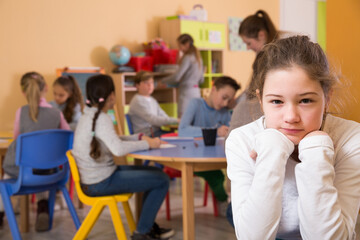 Portrait of sad brunette girl and children drawing in classroom