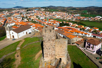 View from drone of two ruined towers of ancient walled fortified Castle of Mogadouro on green hill on background of townscape on spring day, Portugal