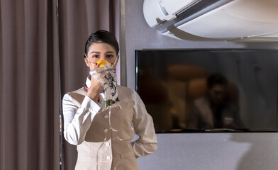 Asian female cabin crew demonstrate how to use oxygen mask on board