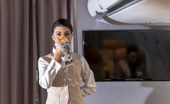 Asian Female Cabin Crew Demonstrate How To Use Oxygen Mask On Board