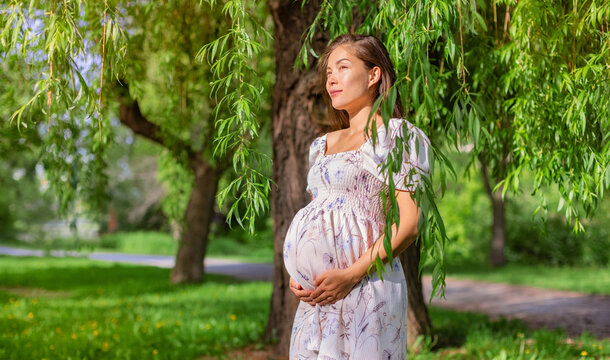 Pregnant Asian beauty woman in summer park. Natural pregnancy girl wearing maternity dress clothes in nature landscape background