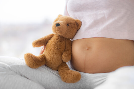 Pregnant woman belly closeup with baby toy teddy bear plush. Skincare, stretch mark, common skin problems of pregnancy. Healthy expecting girl, maternity clothes