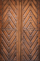 Old brown door made of natural wood with a diamond pattern in the rays of daylight.