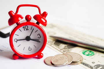Alarm clock with coins on US dollar banknotes, finance installment loan time.