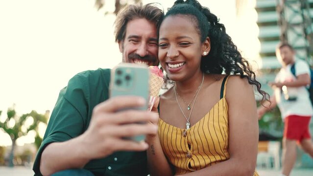 Close up of happy man and smiling woman watching video on smartphone. Close-up of a joyful young interracial couple browsing photos on a mobile phone on urban city background