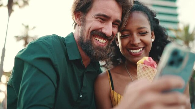 Close up portrait of happy man and smiling woman watching video on smartphone. Close-up of joyful young interracial couple browsing photos on mobile phone on urban city background