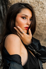 Close up portrait of  gorgeous asian woman  with red lips  in trendy black leather jacket and sensual black dress posing on rocky background.