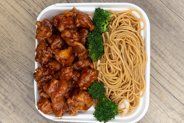 Delicious take out order of crispy breaded chicken with chow mein noodles in a styro foam box