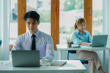 Fototapeta premium The concept of working together for young handsome and beautiful youngsters working on financial accounting and graphing, analyzing, and calculating documents with the laptop on a desk in the office.