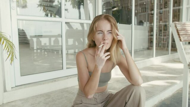 Pretty young woman with vitiligo pigmentation sits on the stairs and smokes 