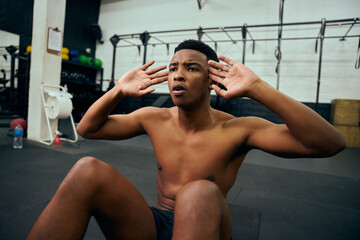 Fototapeta na wymiar Young, topless African American male doing sit-ups on the floor in the gym. Mixed race male personal trainer doing cross training indoors. High quality photo