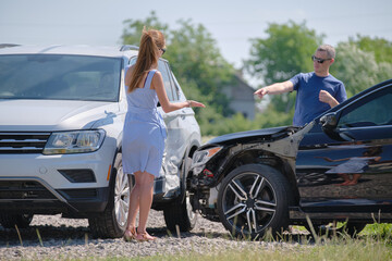 Naklejka premium Angry woman and man drivers of heavily damaged vehicles arguing who is guilty in car crash accident on street side. Road safety and insurance concept