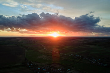 Bright colorful sunset sky with setting sun and vibrant clouds over dark landscape