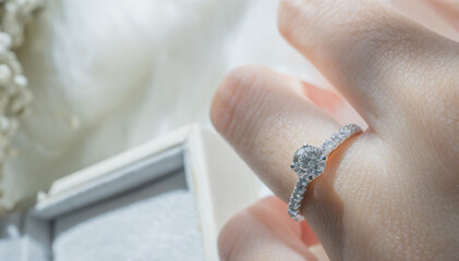 Close up of diamond ring on woman’s finger with  white flower, sunlight and shadow background....