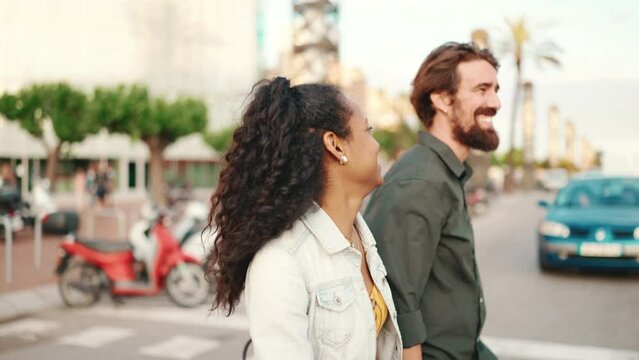 Closeup, happy interracial couple going down the cross the road holding hands and chatting. Close-up of young happy man and woman walking along a crosswalk