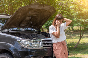 Naklejka premium Woman using mobile phone calling for assistance with broken down car engine on street.