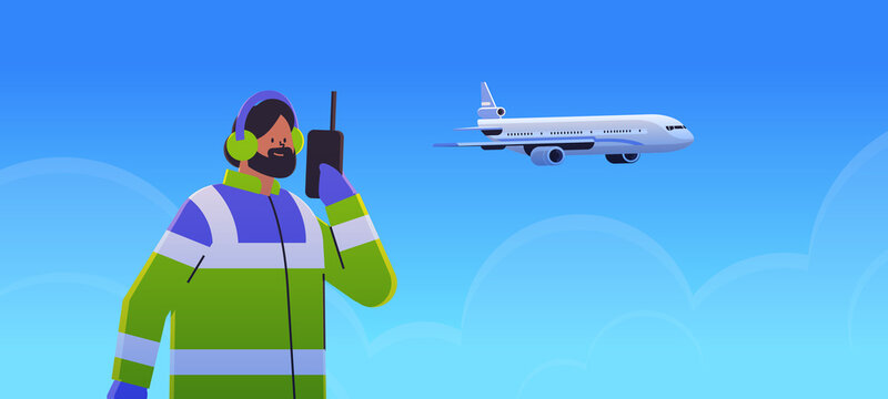 airport worker marshaller man communicating over walkie-talkie with air traffic control while airplane flying in sky