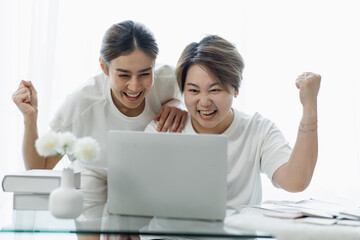 Happy lgbt gay couple of Asian women having fun using a computer laptop at home - LGBT lesbian...