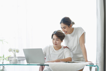 Happy lgbt gay couple of Asian women having fun using a computer laptop at home - LGBT lesbian relationship, Asian LGBTQ female lesbian concept.