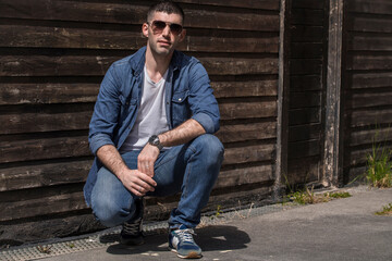 young man with sunglasses squatting on the wall