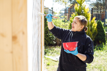 Creative and concentrating, smiling woman painting grid cell fence in countryside by brush in white...
