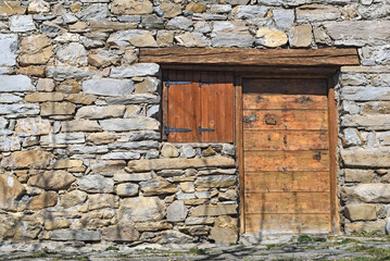 Fototapeta na wymiar facade of old alpine chalet in stone with wooden door and shutters closed