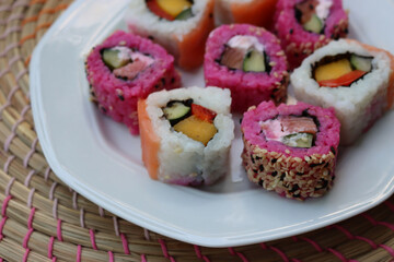 Japanese salmon sushi colored with beetroot juice with inside out rolls with fruits and vegetables on plate on wooden table