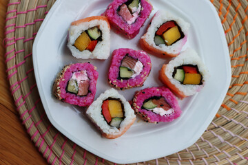 Japanese salmon sushi colored with beetroot juice with inside out rolls with fruits and vegetables on plate on wooden table