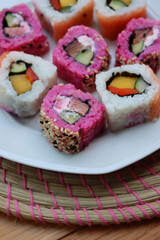 Japanese salmon sushi colored with beetroot juice with inside out rolls with fruits and vegetables on plate on wooden table
