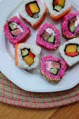 Japanese salmon sushi colored with beetroot juice with inside out rolls with fruits and vegetables on plate on wooden table