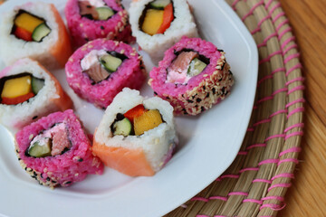 Japanese salmon sushi colored with beetroot juice with inside out rolls with fruits and vegetables on plate on wooden table