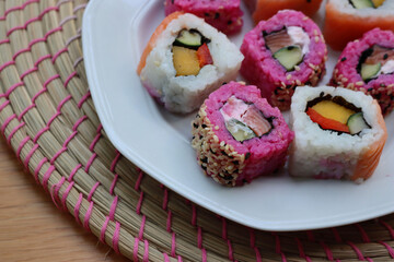 Japanese salmon sushi colored with beetroot juice with inside out rolls with fruits and vegetables on plate on wooden table