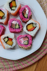 Japanese salmon sushi colored with beetroot juice with inside out rolls with fruits and vegetables on plate on wooden table