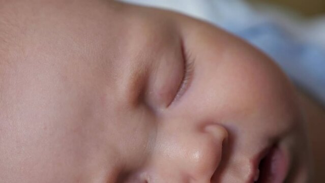 Adorable newborn girl with closed eyes sleeps peacefully in bed. Portrait of little baby with plump cheeks at daytime sleep in nursery, close-up